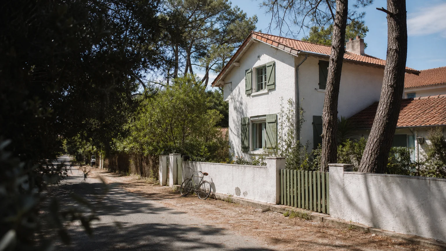 Maison blanche aux volets verts dans une rue arborée de la côte landaise
